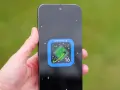 Dłoń trzyma smartfon z ikoną Android 16 na ekranie, przypominającą zielony kryształ na tle kosmosu.