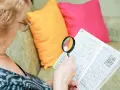 Starsza pani z lupą rozwiązuje krzyżówkę, przeglądając historię swoich rozwiązań.
