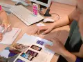 Dwie osoby przeglądają ofertę telefonów komórkowych. Na biurku leży klawiatura, myszka, skaner i katalog z produktami. Jedna z osób pisze coś na formularzu.