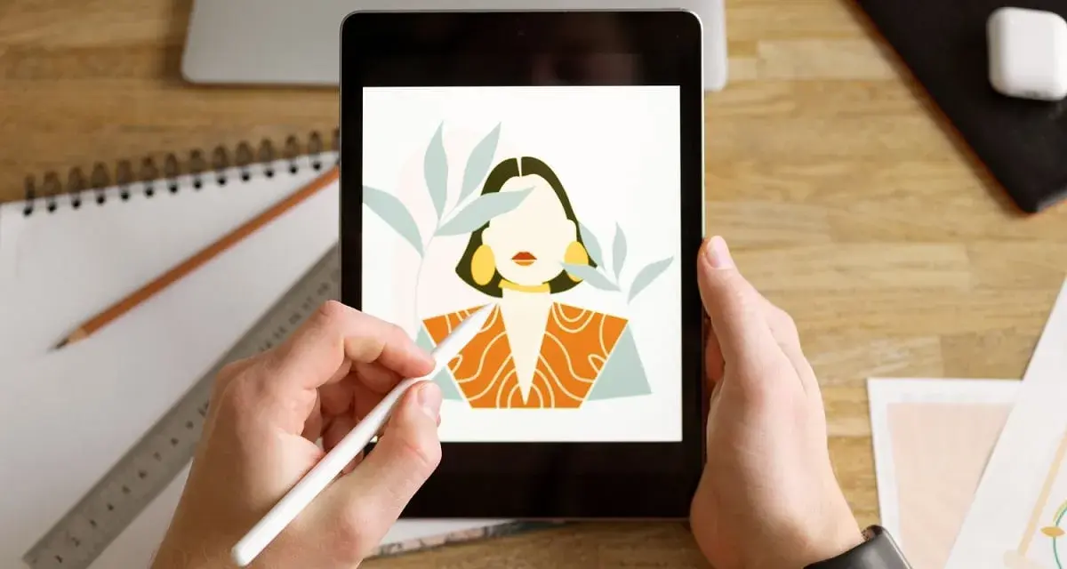 Ręce trzymają tablet, na którym wyświetla się portret kobiety w stylu procreate android. Obok leży notatnik i ołówek.