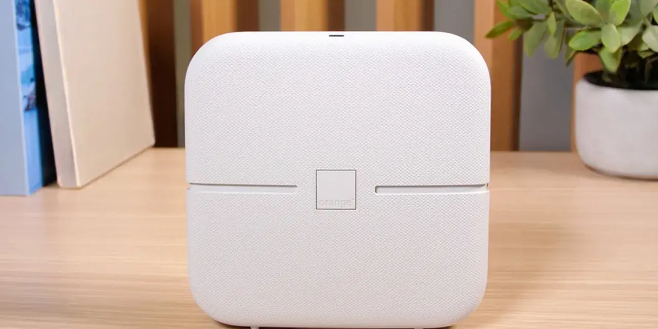 Biały router funbox 7 Orange, z logo operatora, stoi na drewnianym biurku obok książek i rośliny.