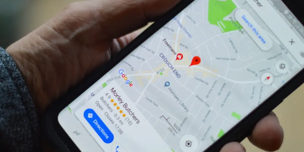 Dłoń trzyma smartfon z mapą Google. Widoczne są google maps współrzędne i wyszukiwanie "butcher".