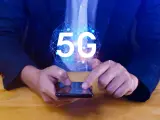 Dłoń na smartfonie, symbol 5G nad nim. Dowiedz się, jak wyłączyć 5G w telefonie, aby kontrolować połączenie.