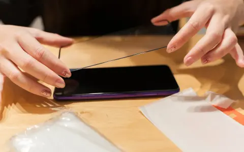 Dłonie przygotowują ochronę wyświetlacza play. Nakładanie szkła hartowanego na ekran telefonu.
