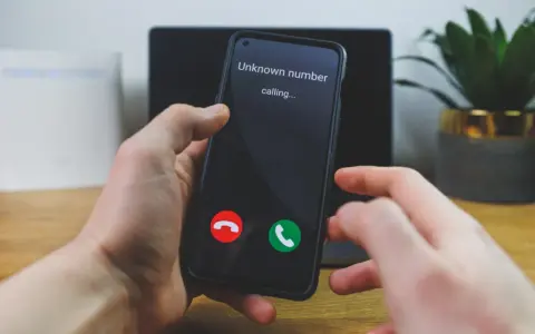 Dłoń trzyma telefon, na ekranie którego widnieje komunikat "Unknown number calling...". Czy odbierze, gdy numer prywatny dzwoni?
