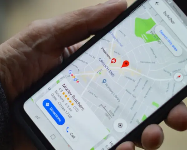 Dłoń trzyma smartfon z mapą Google. Widoczne są google maps współrzędne i wyszukiwanie "butcher".