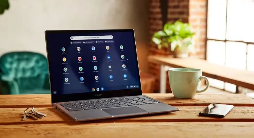 Laptop z systemem Chrome OS Flex, gotowy do pobrania, na drewnianym stole obok kubka i kluczy.