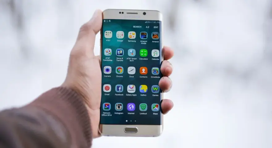 Dłoń trzymająca złoty telefon Samsung z widocznymi ikonami aplikacji.