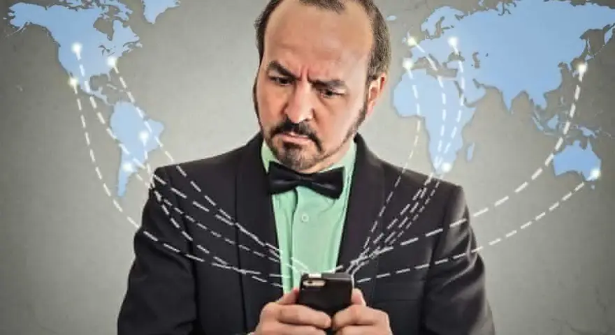 Mężczyzna w garniturze z telefonem, zastanawia się, co to roaming. Mapa świata z połączeniami sugeruje globalną sieć.