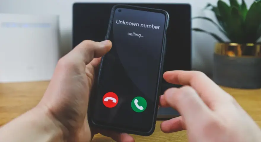 Dłoń trzyma telefon, na ekranie którego widnieje komunikat "Unknown number calling...". Czy odbierze, gdy numer prywatny dzwoni?