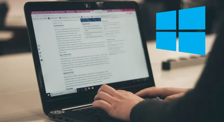 Ręce piszą na klawiaturze laptopa, na ekranie widać artykuł o malowaniu dachu. Obok logo Windows.