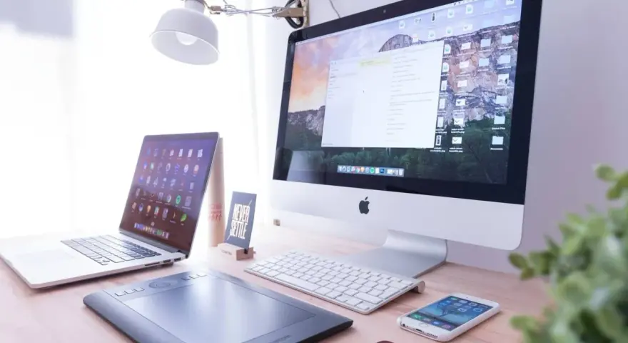 Biurko z iMac, laptopem, tabletem graficznym i telefonem. Na ekranie komputera widać okno programu Adobe Dreamweaver, gotowe do pracy nad stroną.