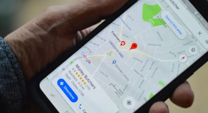 Dłoń trzyma smartfon z mapą Google. Widoczne są google maps współrzędne i wyszukiwanie "butcher".