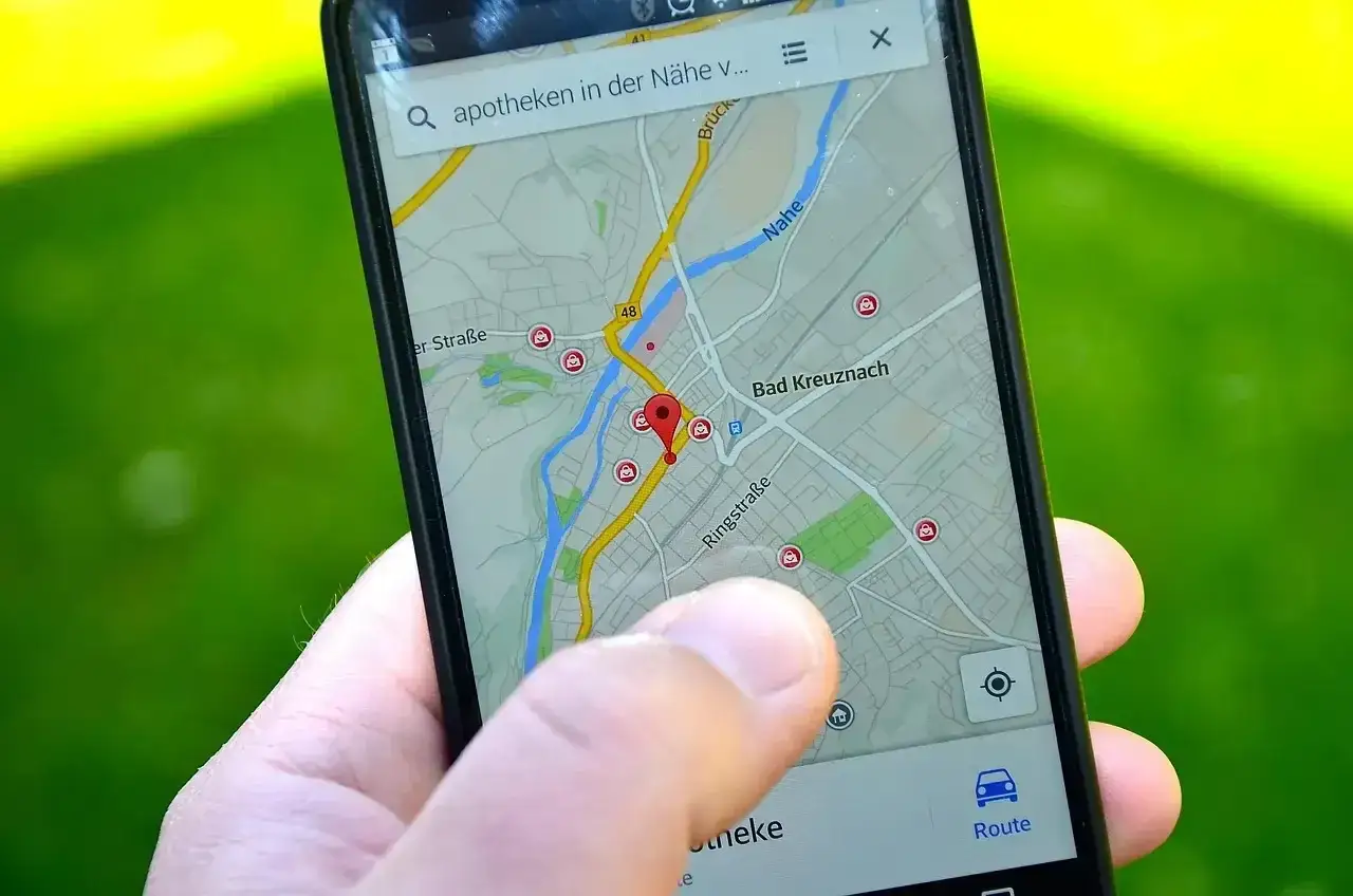 Palec dotyka ekranu telefonu z mapą, szukając aptek w pobliżu. Nawigacja prowadzi przez Bad Kreuznach.