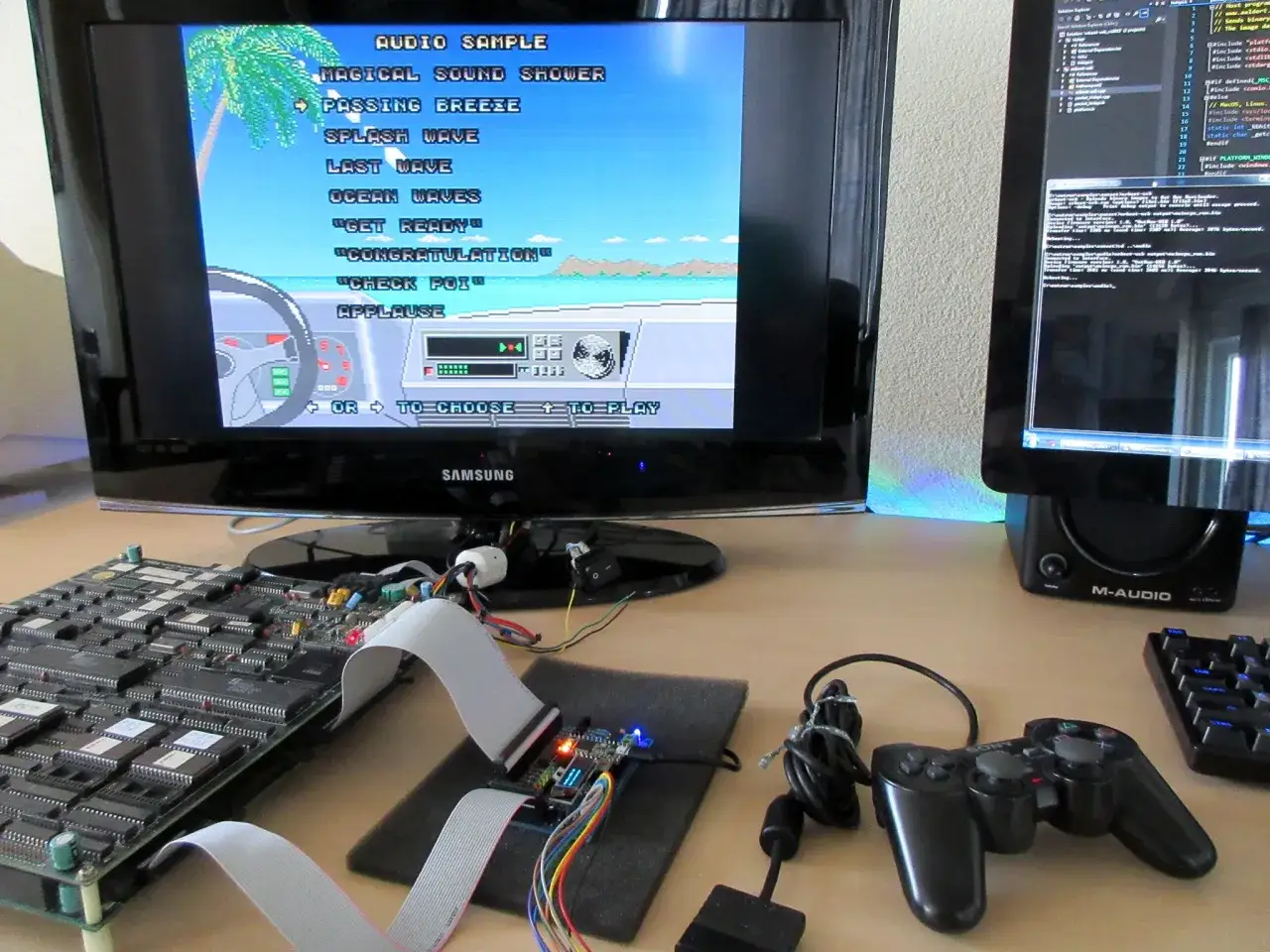 Na biurku stoi monitor z grą uruchomioną na emulatorze PS2, obok niego kontroler i płytka z układami.