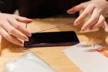 Dłonie przygotowują ochronę wyświetlacza play. Nakładanie szkła hartowanego na ekran telefonu.