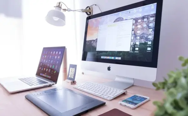 Biurko z iMac, laptopem, tabletem graficznym i telefonem. Na ekranie komputera widać okno programu Adobe Dreamweaver, gotowe do pracy nad stroną.